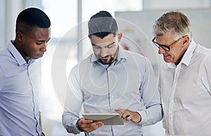 I like that version of it. a group of businessmen making use of a tablet while standing in the office at work.