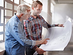 I like what youve done here. two male architects discussing blueprints while standing indoors.