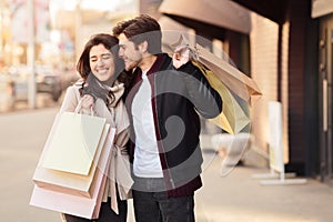 I`ll buy it. Happy couple with shopping bags, man whispering to woman