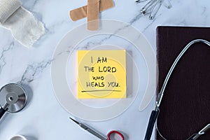 I am the LORD who heals you, handwritten text verse on note with medical tools and holy bible book, top view