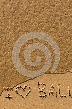 I love Bali - phrase written by hand on the beach with soft waves. Travel.