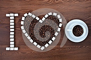 I love coffee. Heart of coffee beans and sugar cubes and white cup and saucer filled with coffee beans on wooden background.