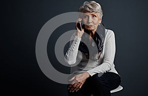 I love this contraption. Studio shot of a cheerful elderly woman sitting down and talking on her cellphone.