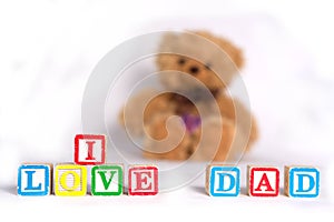 I love dad, photo with brown soft toy bear on the white background. The words are made with kids cubes, colorful letters.
