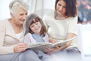 I love fairytales. a little girl sitting with her mother and grandmother and reading a book.