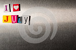 I Love July written with color magazine letter clippings on metal background. Concept of summer time and vacation. Empty