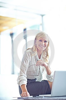 I love my job. Portrait of a smiling business woman sitting on her desk with her laptop in front of her.