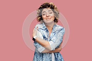 I love my self. Portrait of satisfied young woman with curly hairstyle in casual blue shirt standing, looking at camera, smiling