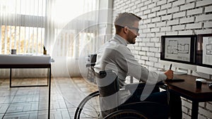 I love my work. Side view of young smiling male engineer or architect in a wheelchair using stylus pen and digital