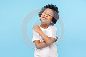 I love myself. Portrait of adorable optimistic little boy with curls embracing himself and smiling