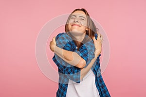 I love myself! Portrait of charming girl in checkered shirt hugging herself tightly and smiling with pleasure