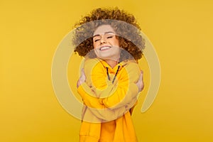 I love myself! Portrait of self-satisfied egoistic curly-haired woman in urban style hoodie embracing herself