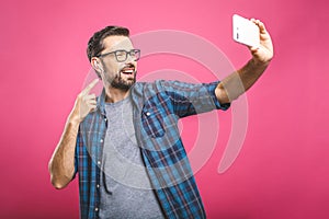 I love selfie! Handsome young man in shirt holding camera and making selfie and smiling while standing against pink background.