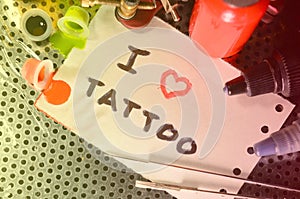 I love tattoo. The text is written on a small sheet of paper among various equipment for tattooing