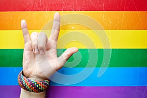 `I love you` in American sign language ASL which shows a man`s hand on the background of the flag of LGBT LGBTQ community