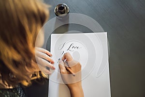 I love you. Calligrapher Young Woman writes phrase on white paper. Inscribing ornamental decorated letters. Calligraphy