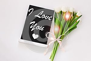 I love You card message sign on black chalkboard with tulip flowers on white background flatlay.Blackboard greeting text