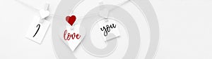 I love you - Clothes pegs with red wooden hearts and paper notes hang on rope isolated on white texture background panorama banner
