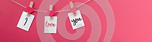 I love you - Clothes pegs with wooden hearts and paper notes hang on rope isolated on pink texture background panorama banner long