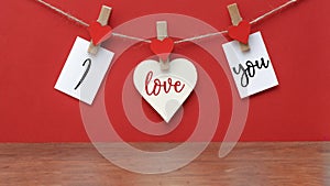 I love you - Clothes pegs with wooden hearts and paper notes hang on rope isolated on red texture background, with space for text