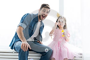 I love you, dad! Handsome young man at home with his little girl are having fun and blowing soap bubbles. Happy Father`s