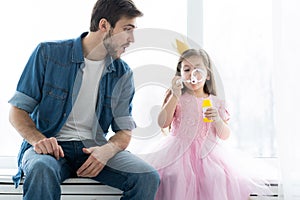 I love you, dad! Handsome young man at home with his little girl are having fun and blowing soap bubbles. Happy Father`s