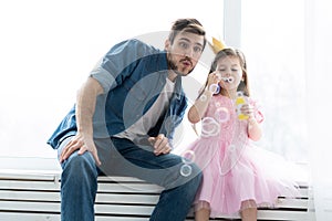 I love you, dad! Handsome young man at home with his little girl are having fun and blowing soap bubbles. Happy Father`s