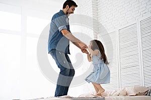 I love you, dad! Handsome young man at home with his little girl are having fun and jumping on bed. Happy Father`s Day!