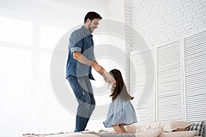 I love you, dad! Handsome young man at home with his little girl are having fun and jumping on bed. Happy Father`s Day!