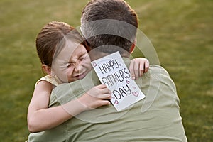 I love you, daddy. Cute happy little girl, small daughter hugging her father and giving him postcard on holiday