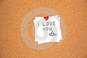 I love you handwriting lettering on 1 white papers pinned with 2 big red heart pegs and one small red heart pegs on cork board