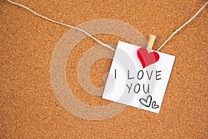 I love you with heart sign on white paper pinned with heart pegs on cork board