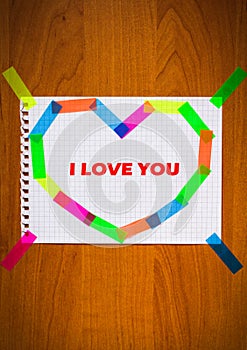 I love you inscription red color card sheet of notepad paper in heart shape on the wooden background bright stickers