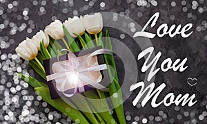 I love You Mom card message sign. White tulip flowers and black gift box on dark background with bokeh lights flat lay