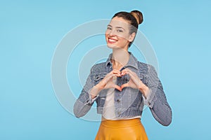 I love you! Portrait of amorous cheerful fashionably dressed woman with hair bun showing heart shape with hands