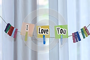 I love you. Text message on colorful paper notes with clips hanging on rope on white curtain background. Notes on sticky note