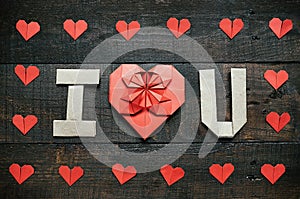 I LOVE YOU, U folded letters. Red origami paper hearts frame on dark brown aged wood background. Valentines day horizontal