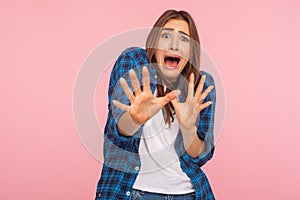 I`m afraid! Portrait of shocked scared girl in checkered shirt screaming in horror and fear, keeping hands raised