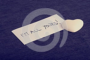 I'm all yours handwritten on a white card with a cream colored h photo