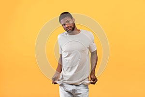 I'm broke. Unemployed african american man showing empty turned out pockets, standing over yellow background