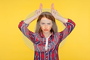 I`m a cow. Portrait of angry menacing ginger girl in checkered shirt showing bull horns on head, threatening to attack