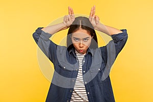 I`m dangerous! Portrait of girl in denim shirt threatening to attack with bull horns gesture over head