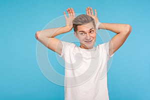 I`m rabbit! Portrait of funny carefree man in casual white t-shirt making bunny gesture with hands