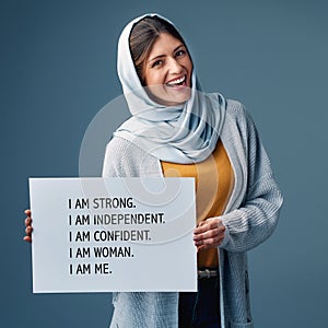 I am me. Studio portrait of an attractive young woman holding up a sign stating who and what she is against a grey