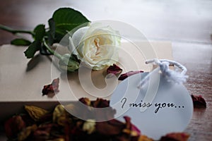 I miss you. Romantic note message written on white paper tag label with background of white rose lying  and dried petals scattered