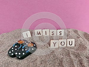 I miss you written on wood blocks on the sand at the beach with a pair of blue flip flops
