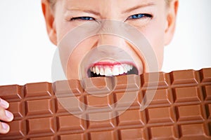 I must eat it all. Crazed young woman biting into a huge piece of chocolate.