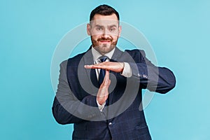 I need more time. Portrait of frustrated brunette man with beard in dark suit showing time out