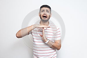 I need more time. Portrait of pleased handsome bearded young man in striped t-shirt standing with time out gesture and looking at