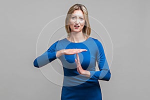 I need more time. Portrait of young woman showing time out or pause gesture. indoor studio shot isolated on gray background